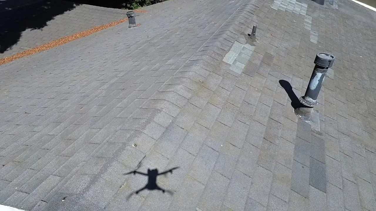 Our drone directly over a Santa Barbara shingle roof — vents, pipe jacks, and past patch repairs visible, drone shadow on the field