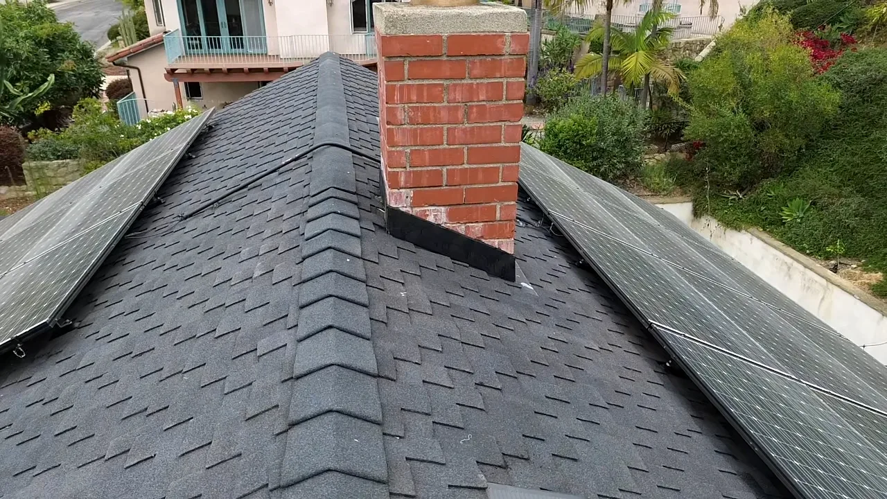 Drone view of an asphalt shingle roof with solar panels and a brick chimney in Santa Barbara